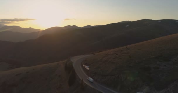 Vit transport van kör på bergsvägen på kvällen. Sista solstrålarna skiner över bergstoppar — Stockvideo