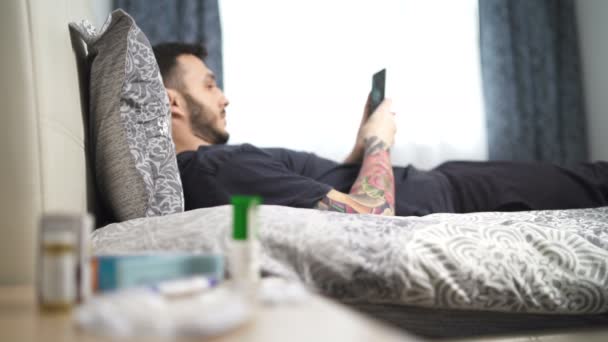 Βαρετός άνθρωπος ξαπλωμένος στο κρεβάτι και χρησιμοποιώντας το smartphone του κατά τη διάρκεια καραντίνας ή κλείδωμα — Αρχείο Βίντεο