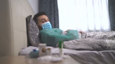 Virüs bulaşmış öksüren bir adam yatakta uzanıp vücut ısısını ölçüyor.