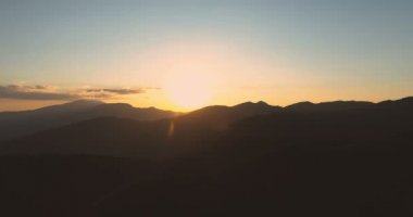 Karanlık dağ tepelerinin üzerinde açık gökyüzü ile altın günbatımının panoramik manzarası