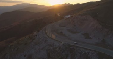Siyah araba gün batımında ıssız dağ yolunda gidiyor. Baharda yolculuk.