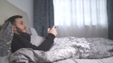 Hasta genç adam yatağından video oyunları oynuyor. Öksüren ve yatakta yatan adam.