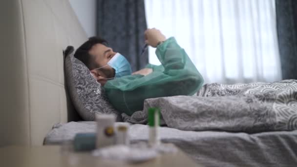 Uomo malato con maschera facciale e tuta medica che misura la sua temperatura con termometro ascella — Video Stock