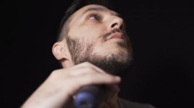 Genç adam sakalını tıraş etmek için tıraş bıçağı kullanıyor. Siyah arkaplanda izole