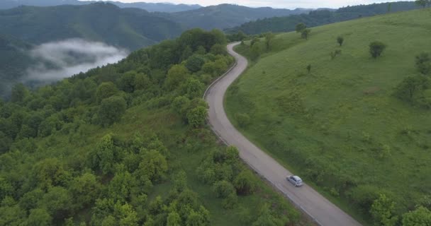 Dron dağlardaki yeşil tepelerden geçen dolambaçlı yolda giden arabayı takip ediyor. — Stok video