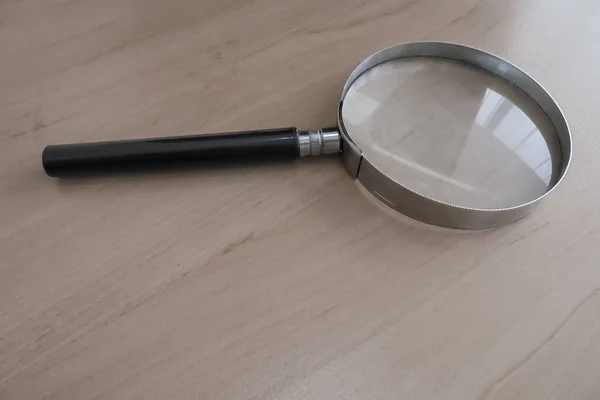 a round glass magnifier in a metal frame with a black wooden handle lies on the table