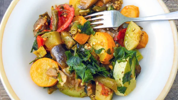 Beyaz yuvarlak bir tabakta çatalla pişirilmiş sebzeler. haşlanmış sarı ve beyaz kabak, patlıcan, domates, kuşkonmaz fasulyesi, dolmalık biber ve yeşil maydanoz. Yukarıdan görünüm