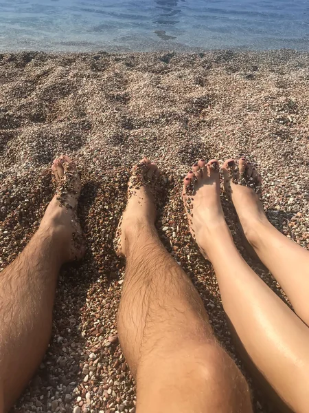 male hairy and female smooth legs on the beach of small pebbles by the water