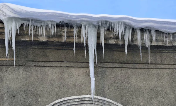 Ghiaccioli primaverili appesi al tetto coperto di neve — Foto Stock