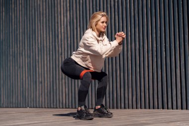 Sarışın, güzel bir kadın dışarıda lastik bantla egzersiz yapıyor. Bahar sporu aktiviteleri dışarıda.