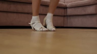 Kanepenin yanındaki büyük bir oturma odasında dans eden bir kızın ayakları var. Beyaz çorap ve sandalet giyiyor ve balerin gibi hareket ediyor. Dans okulu için harika bir konsept..