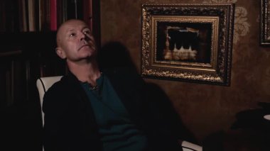 Yaşlı bir adam beyaz deri bir koltukta oturuyor ve bir şeyi yansıtıyor. Duvarda altın çerçeveli harika bir tablo var. Harika bir sanat ve sosyal konsept..