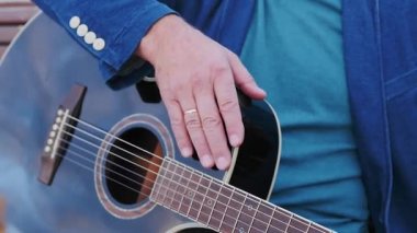 Bir gitarist enstrümanını eliyle tıklatıyor. Yan tarafında siyah 6 telli akustik gitar var. Gitar mağazası ya da müzik atölyesi için harika bir konsept..