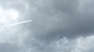 Küçük bir uçak, seyirciyi eğlendirmek için şehrin yukarısında farklı halkalar, saltolar ve diğer başarılar yapıyor. Gökyüzü gri ve bulutlu.