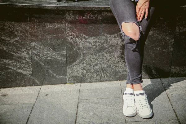 Menina fica na calçada, em calças rasgadas e tênis brancos — Fotografia de Stock