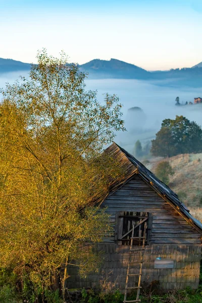 Bela paisagem de outono durante o nascer do sol com cabana velha e neblina no vale com montanhas, Romênia — Fotografia de Stock