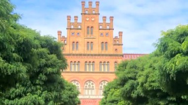 Chernivtsi Ulusal Üniversitesi 'nin güzel tarihi binası Ukrayna' da yeşil ağaçlı ve çalılıklı kırmızı tuğlalı dini seminer.