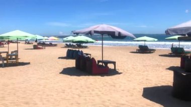 Endonezya, Bali 'de güneşli yatakları, şemsiyeleri ve Legian plajı olan geniş kumlu bir sahil. 4k video.