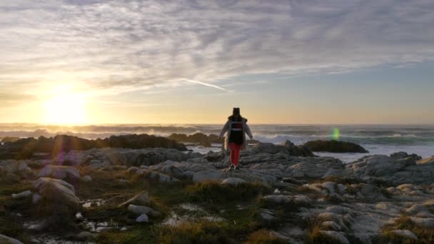 Mujer caucásica mayor madura caminando hacia adelante en gorro de chaqueta de plumón en el mar, con olas lentas costa del océano puesta de sol o el fondo del amanecer — Vídeos de Stock