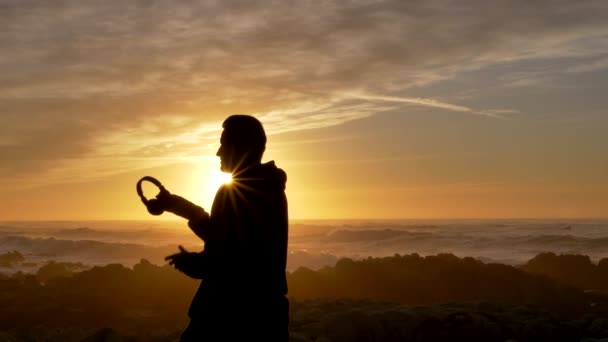 Hombres en cámara lenta usando auriculares inalámbricos antes de entrenar beckground puesta de sol escénica en la costa pacífica de California — Vídeo de stock