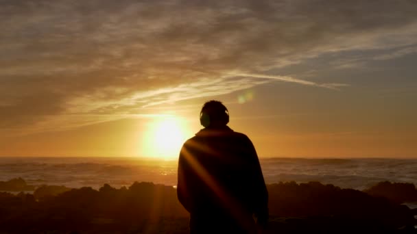 Muži kráčející ve zpomaleném filmu na sobě bezdrátové sluchátka sledování krásné vlny beckground scénický západ slunce na pobřeží Kalifornie Pacifik — Stock video