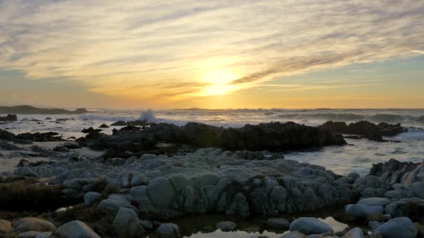 Slow motion pan right Pacific Ocean Waves rolling in and break on a rocky coast under a sunset sky at Pacific Grove, California on the Monterey Peninsula at stormy weather — Stock Video