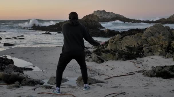 Muži bojovník mnich cvičí siluetu tai chi karate kung Fu na skalnatém obzoru při západu slunce nebo východu slunce. Umění sebeobrany. Silueta na pozadí dramatických epických vln na pobřeží Pacifiku — Stock video