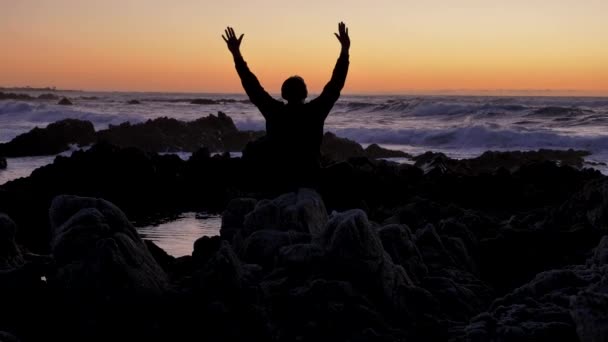 Mannen die yoga beoefenen op de rotsachtige stenen horizon bij zonsondergang of zonsopkomst. Kunst van zelfverdediging. Silhouet op een achtergrond van dramatische epische golven aan de Stille Oceaan — Stockvideo