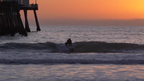 Surfer bei malerischem orange-rosa Sonnenuntergang mit epischen Lichtstrahlen und Sonnenfackel Holzsteg in San Clementa Kalifornien — Stockvideo
