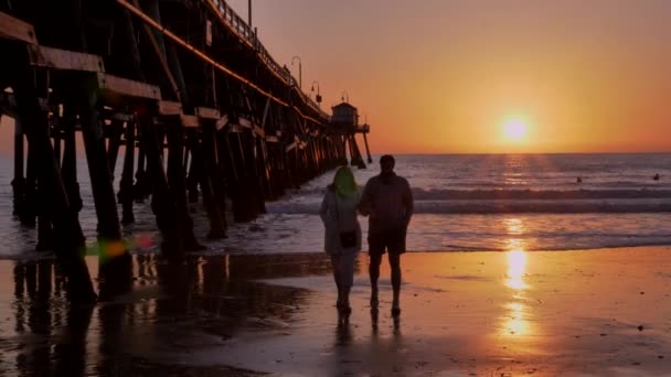 Couple walking at Scenic orange pink Sunset with epic rays of light and sun flare wooden pier in San Clementa California — Stock Video