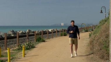 Yakışıklı, genç bir adam, lacivert gömlekli, şortlu ve gözlüklü bir adam California sahilindeki San Clemente Linda Lane Parkı 'nda telefona bakıyor..