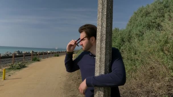 Yakışıklı, genç bir adam, lacivert gömlekli, şortlu, gözlüklü gülümseyen bir adam California sahilinde fenerle yürüyor ve Linda Lane Parkı 'nda dönüyor.. — Stok video