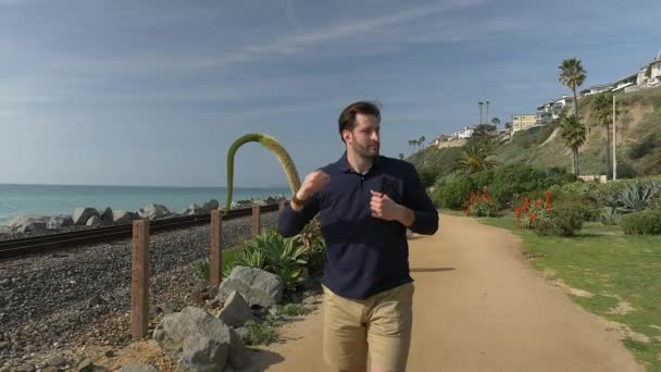 Egy jóképű, fiatal fickó, egy férfi tengerészkék ingben, rövidnadrágban és szemüvegben felnéz Kalifornia partjainál San Clemente Linda Lane parkban.. — Stock videók