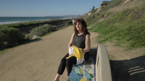 Mulher feliz Belo dia de verão ensolarado sentado no banco colorido na costa do oceano. Viagem férias aposentadoria estilo de vida conceito Califórnia Orange County San clemente — Vídeo de Stock