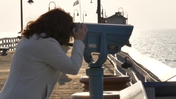 Femme regardant à travers une pièce opéré jumelles au bord de l'océan jetée — Video