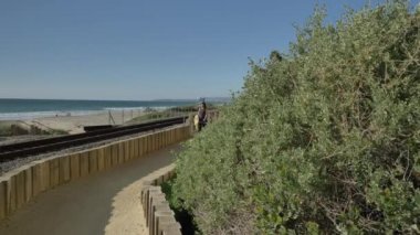 Aktif kıdemli kadın California San Clemente Calafia plajında yaz günü okyanusa yakın yaya yolu ahşap köprüde yürüyor. Orange County yaşam tarzı