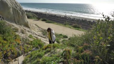 Kaliforniya San Clemente Calafia plajında yaz günü okyanusa yakın yaya yolunda güzel manzaralarla yürüyen aktif kıdemli bir kadın. Orange County yaşam tarzı