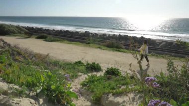 Kaliforniya San Clemente Calafia plajında yaz günü okyanusa yakın yaya yolunda güzel manzaralarla yürüyen aktif kıdemli bir kadın. Orange County yaşam tarzı