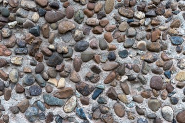 Beton alçı, bir sürü pürüzsüz nehir taşıyla birleşmiş. Dekoratif duvar.