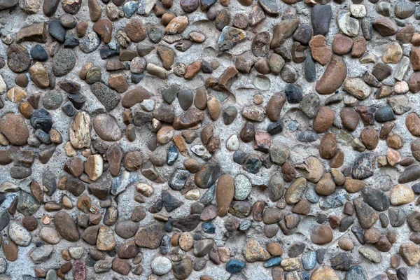 Beton alçı, bir sürü pürüzsüz nehir taşıyla birleşmiş. Dekoratif duvar.