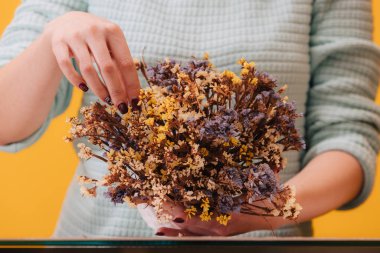 Kurumuş kır çiçekleri. Beyaz bir vazoda bir sürü küçük mavi ve sarı çiçek var. Çiçekçi kız buketi düzeltiyor..