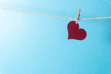 Mavi arka planda küçük bir mandalla ipte sallanan bordo bir kalp..