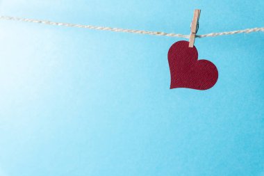 Mavi arka planda küçük bir mandalla ipte sallanan bordo bir kalp..