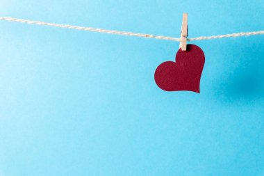 Mavi arka planda küçük bir mandalla ipte sallanan bordo bir kalp..