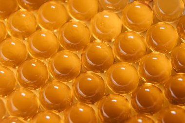 Balık yağı kapsülleri. Kırmızı-turuncu renkli birçok yuvarlak tablet.