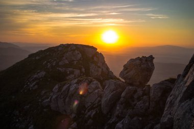 Karpat kayalık dağlarının karanlık siluetleri ve büyük sarı güneşli günbatımı gökyüzü.