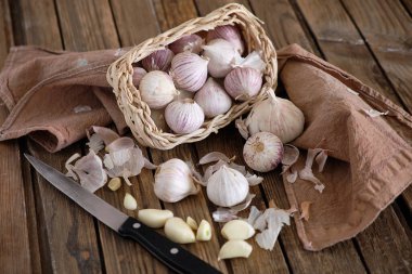 Beyaz, yuvarlak sarımsak sepetin içinde kahverengi ahşap arka planda koyu bir peçeteyle yatıyor. Yanında da sarımsaklı karanfilli bir bıçak var. Yakın plan fotoğraf.