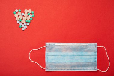 Kırmızı zemin üzerinde haplar ve solunum maskesiyle dolu bir kalp.