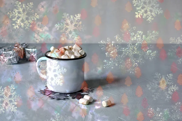 Beyaz metal bardak kakao ya da masa üzerinde marşmelov ve arka planda parlak bokeh ışıkları olan sıcak çikolata. Noel evi konsepti