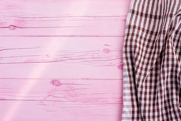 ピンク色の木製のテーブルの上には、白と茶色のチェッカーキッチンタオルや綿のナプキンがあります。上からの眺め。テキストのスペースをコピーします。デザインのレイアウトとして使用できます。料理の背景 — ストック写真